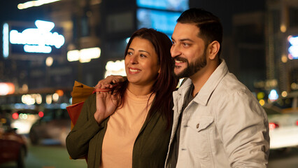 Happy Young Indian Couple shopping at night holding shopping bags