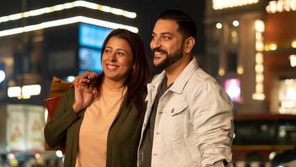 Happy Young Indian Couple shopping at night holding shopping bags