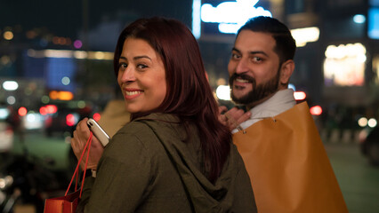 Happy Young Indian Couple shopping at night holding shopping bags
