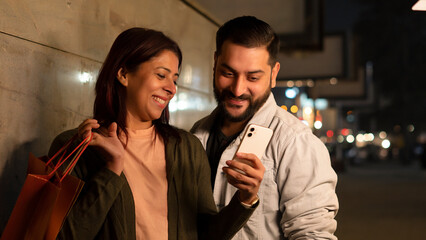 portrait of a couple in the city shopping at night and using smartphone