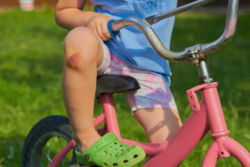 Fototapeta na wymiar a child on a bicycle with an injured knee,a little girl is sitting on a bicycle with a bruised knee