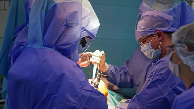 Large surgical team performing knee operation. Doctors in protective suits hold the metal medical tools.