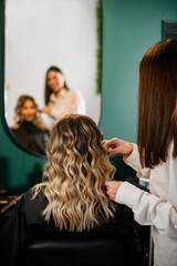 Fototapeta premium great rear view of woman with perfect curl hair and hairdresser in hair salon
