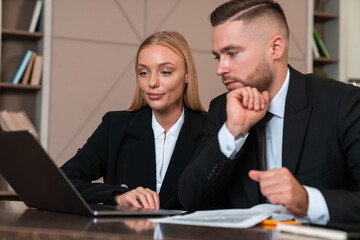 Businesswoman and businessman wearing formal wear sitting working on laptop