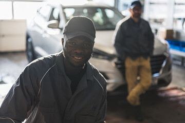 Naklejka premium Mechanics in an auto repair shop posing with a white car for repair in the background. High-quality photo