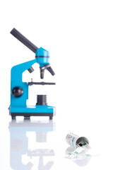 Blood glucose test box with testers spilled in foreground on white reflexive glass with blue blurred microscope in the background. 