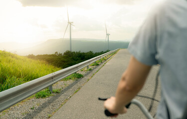 Fototapeta na wymiar Selective focus on wind farm with rearview of person riding a bicycle as foreground. Wind energy. Wind power. Sustainable, renewable energy. Wind turbines generate electricity. Sustainable lifestyle.