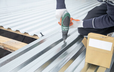 Man installing metal sheet roof by electrical drilling machine.