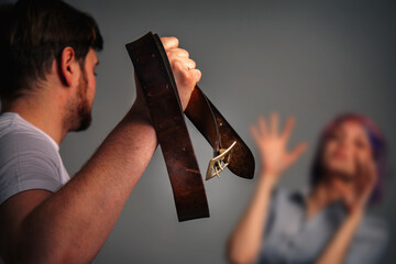 A man beats a woman with a wide leather belt as a symbol of violence in family