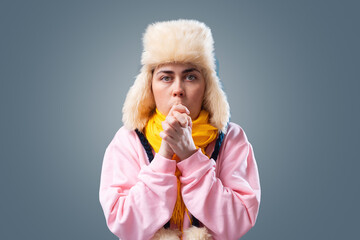 Portrait of young woman in a knitted hat and scarf is trying to keep warm. Gray background. The...