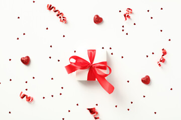 White gift box tied with a red ribbon bow on white background adorned with party streamers,...