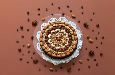 Top view of homemade chocolate cake decorated with different types of nuts and fragrant spices on brown background. Flat lay, close-up, mock up
