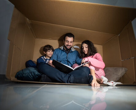fun in a box: father reads book to children playing inside a box