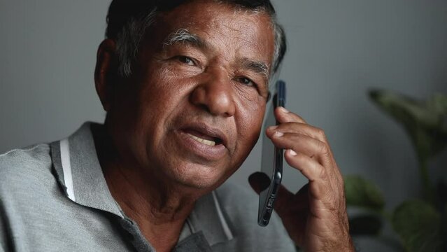 Asian elderly man serious while talking on the phone. Sad old man alone using a smartphone at home