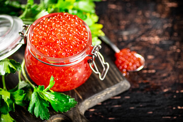 A full glass jar of red caviar on a cutting board. 