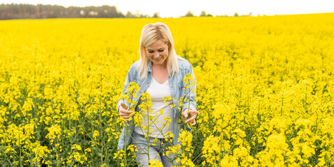 Portrait of attractive woman on blooming rapeseed field with sunset light. Yellow flowers and happy woman