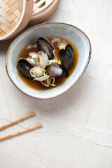 Bowl of mussel and clam miso soup on a light-beige stone background, high angle view, vertical shot with space