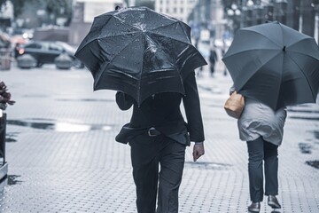 people with umbrellas walk down the street during the rain. people under black umbrellas