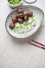 Bowl with asian style rice and teriyaki meatballs, vertical shot on a beige stone background with copy space, high angle view