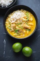 Bowl of yellow curry with fish fillet, vertical shot on a black marble background, high angle view