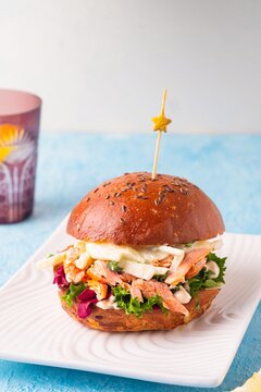 Burger with baked salmon, salad, apple and sauce on a white plate on a blue concrete background. Recipes for burgers.