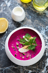 Cold beetroot soup topped with hard-boiled egg and fresh greens, vertical shot on a dark marble background