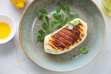 Plate with whole grilled halloumi cheese and fresh greens, middle closeup, elevated view, horizontal shot
