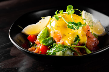 Salad with Boiled Eggs, Salmon, Tomatoes and cucumber in a bowl on black background