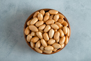 Bowl full of roasted peeled peanuts on bright background