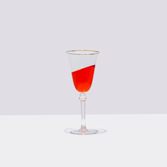 A glass of red cocktail stands straight with the drink  in it is tilted at an angle. Surreal drinking culture, summer party or celebration composition.