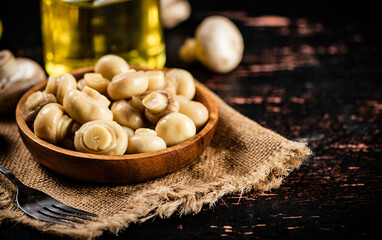 Wooden plate on burlap with pickled mushrooms. 