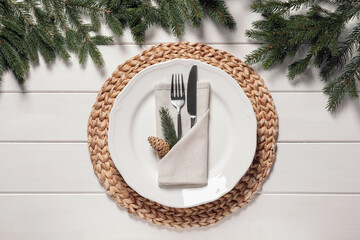 Beautiful festive place setting with cutlery and fir branches for Christmas dinner on white wooden...