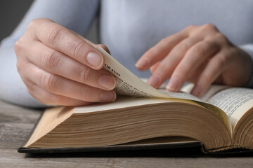 Woman reading Bible at wooden table, closeup