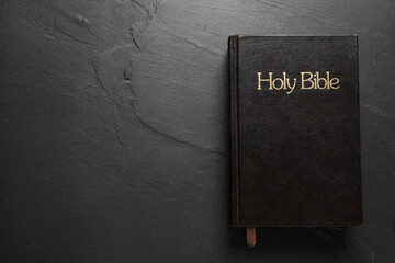 Hardcover Bible on black table, top view with space for text. Religious book