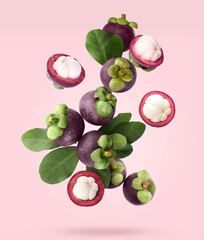 Many ripe mangosteen fruits and leaves falling on light pink background