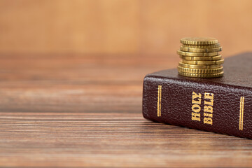 Stack of golden coins on top of holy bible book on a wooden background. Copy space for text. A...