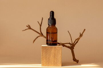 Serum in glass bottle with dropper lid on wooden square stand. Essential oil for care of women's...