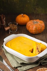 Cottage cheese casserole with pumpkin and raisins in a rectangular baking dish on a brown wooden background.