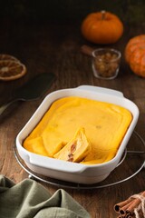 Cottage cheese casserole with pumpkin and raisins in a rectangular baking dish on a brown wooden background.