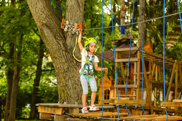 Fototapeta na wymiar Adorable little girl enjoying her time in climbing adventure park on warm and sunny summer day