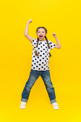 A cheerful and joyful little girl in a polka dot T-shirt and long pigtails on a yellow background.