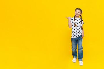 Summer clothes on a beautiful little girl. A child in jeans and a polka dot T-shirt on a yellow background.
