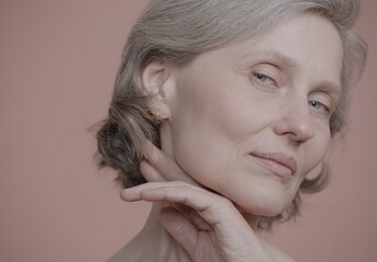 CU Portrait of very beautiful 60s mature senior adult female doing her skincare routine. Studio...
