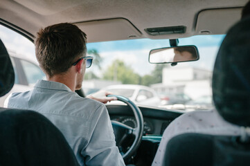 Handsome elegant serious man drives a car. Indoors back view.