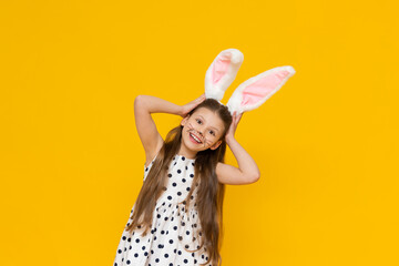 Obraz na płótnie Canvas Masquerade Easter bunny ears on a beautiful little girl on a yellow isolated background. A girl with the face of an Easter bunny.