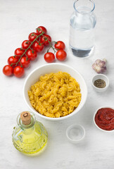 Vegetarian pasta cooking ingredients: pasta, tomatoes, cheese, olive oil, dried oregano, tomato paste, garlic, salt, black pepper, fresh thyme, water on a light gray background, top view.