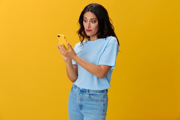 Woman blogger with a phone in her hands in a blue t-shirt and jeans on a yellow background smile signs gestures symbols, online communication and video call, copy space, free background