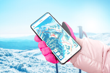 Ski map on phone display in hand with glove. Ski poles and mountain in background