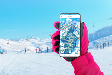 Ski map on smart phone in woman hand with pink glove. Ski and snowboard app concept for route and...