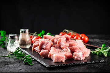 Pieces of raw pork on a stone board with parsley, tomatoes and spices. 